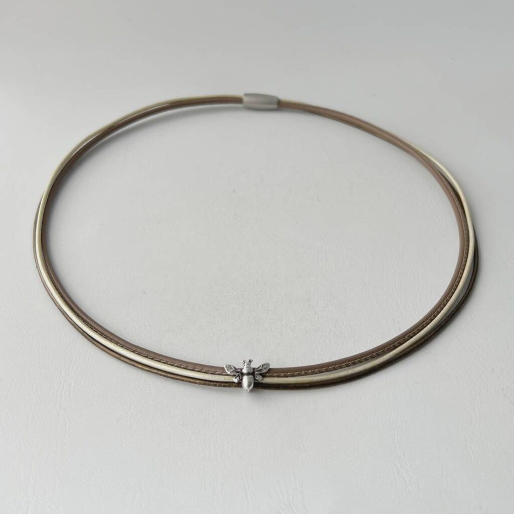 das Ledercollier mit einer Biene in taupe